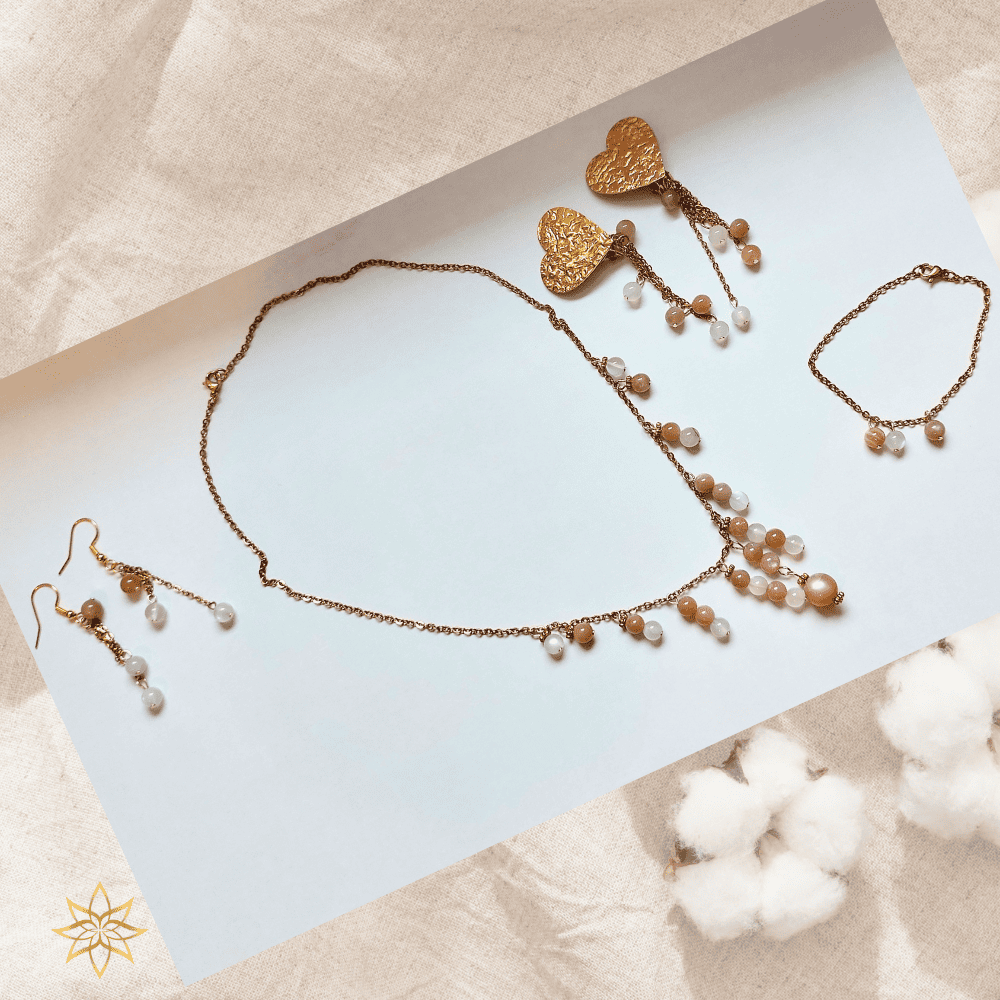 parure lune de miel en pierre de lune et acier inoxydable La parure Lune de miel est une ode à la douceur, à la féminité et à l’intuition. Inspirée par l’énergie apaisante de la lune, elle a été créée comme un bijou-talisman, pensé pour accompagner les femmes dans leur sensibilité, leur équilibre émotionnel et leur reconnexion intérieure. Composée d’un collier, d’un bracelet et de deux paires de boucles d’oreilles (dont une version à clips pour oreilles non percées), cette parure associe la pierre de lune naturelle à l’élégance lumineuse de l’acier inoxydable doré.