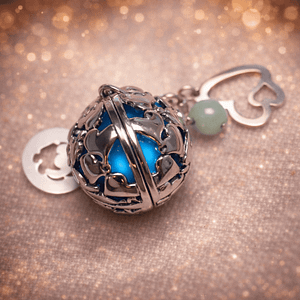 bola de grossesse personnalise Bola de grossesse en acier argenté au design ajouré, sublimé par une pierre bleue lumineuse. Son tintement doux favorise la détente et le bien-être pendant la grossesse. Accompagné de charms délicats (trèfle, cœur ou perle), ce bijou symbolise la protection, la sérénité et l’harmonie. Idéal comme cadeau de grossesse ou bijou de maternité.